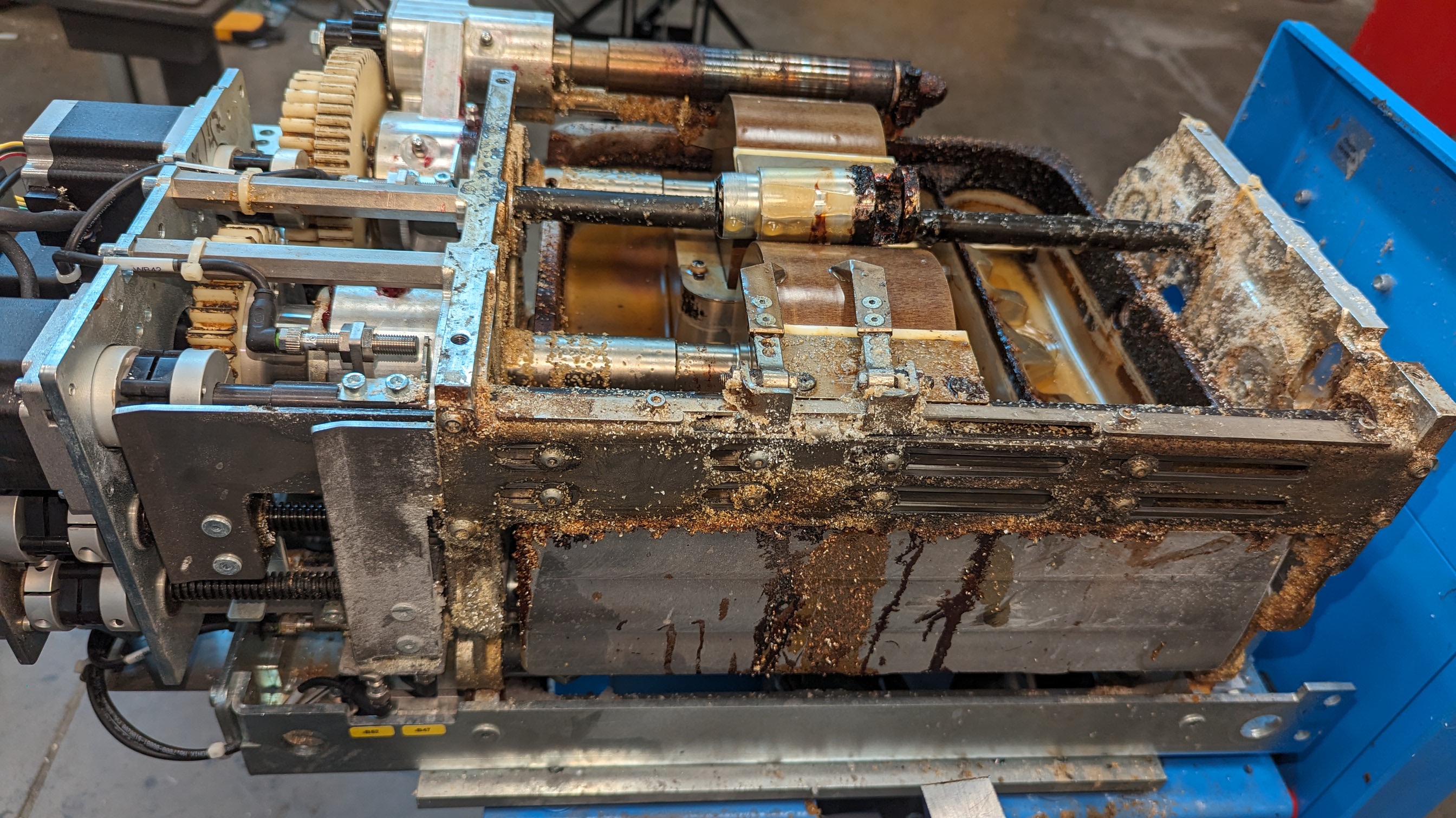 Glue applicator unit side view on service cart — adhesive dripping, rust and scale on all exterior surfaces