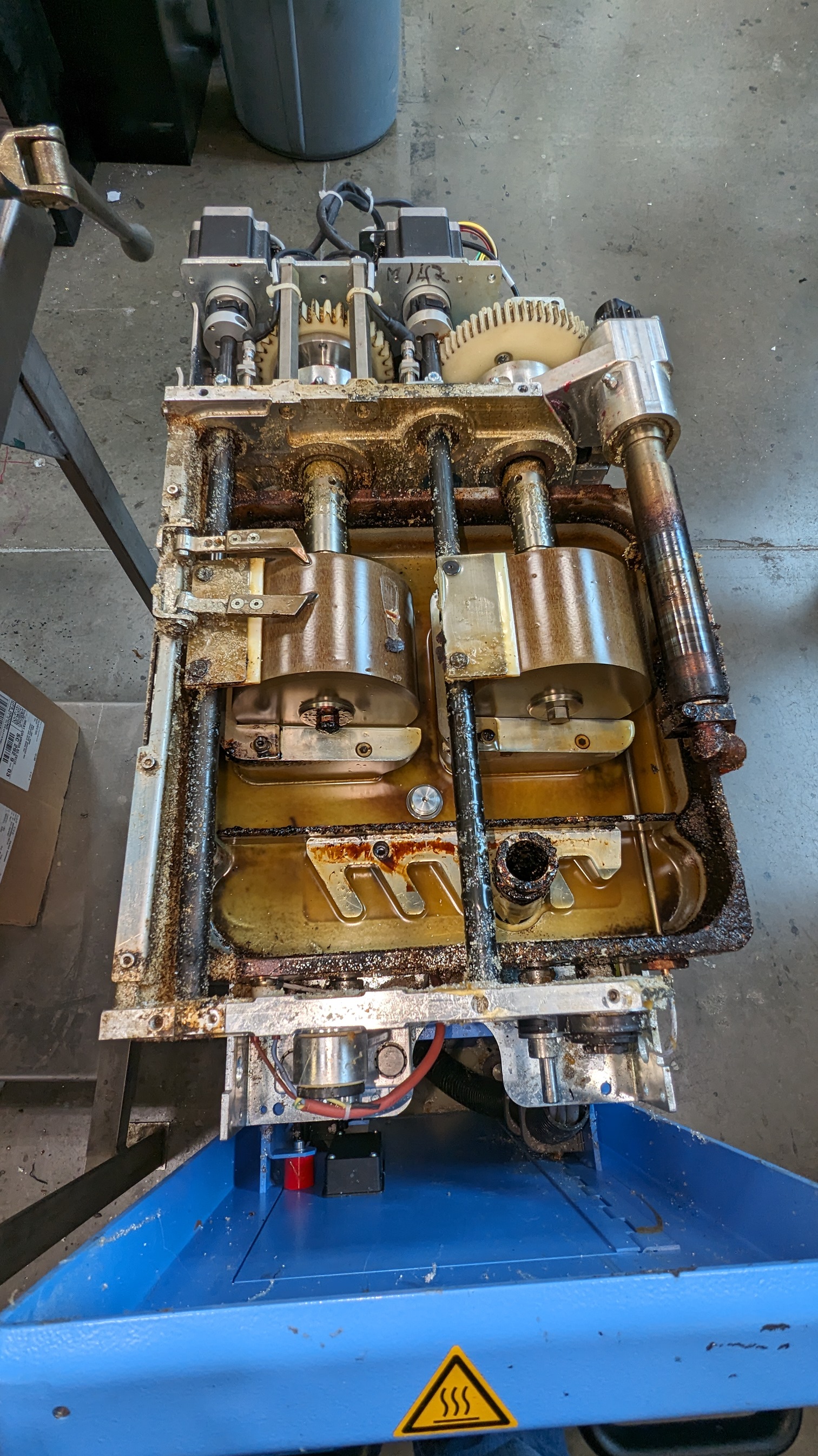 Top-down view of full glue applicator on cart — two adhesive bowls with amber polymerized adhesive, rust throughout