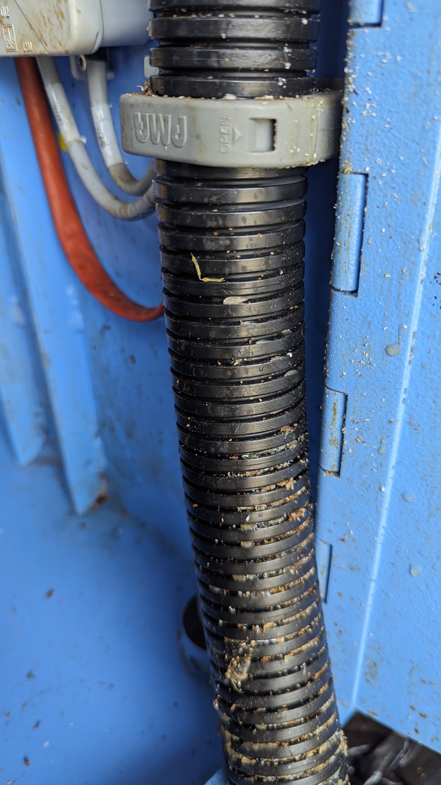 Black corrugated conduit hose caked with white cardboard particulate and adhesive residue — before